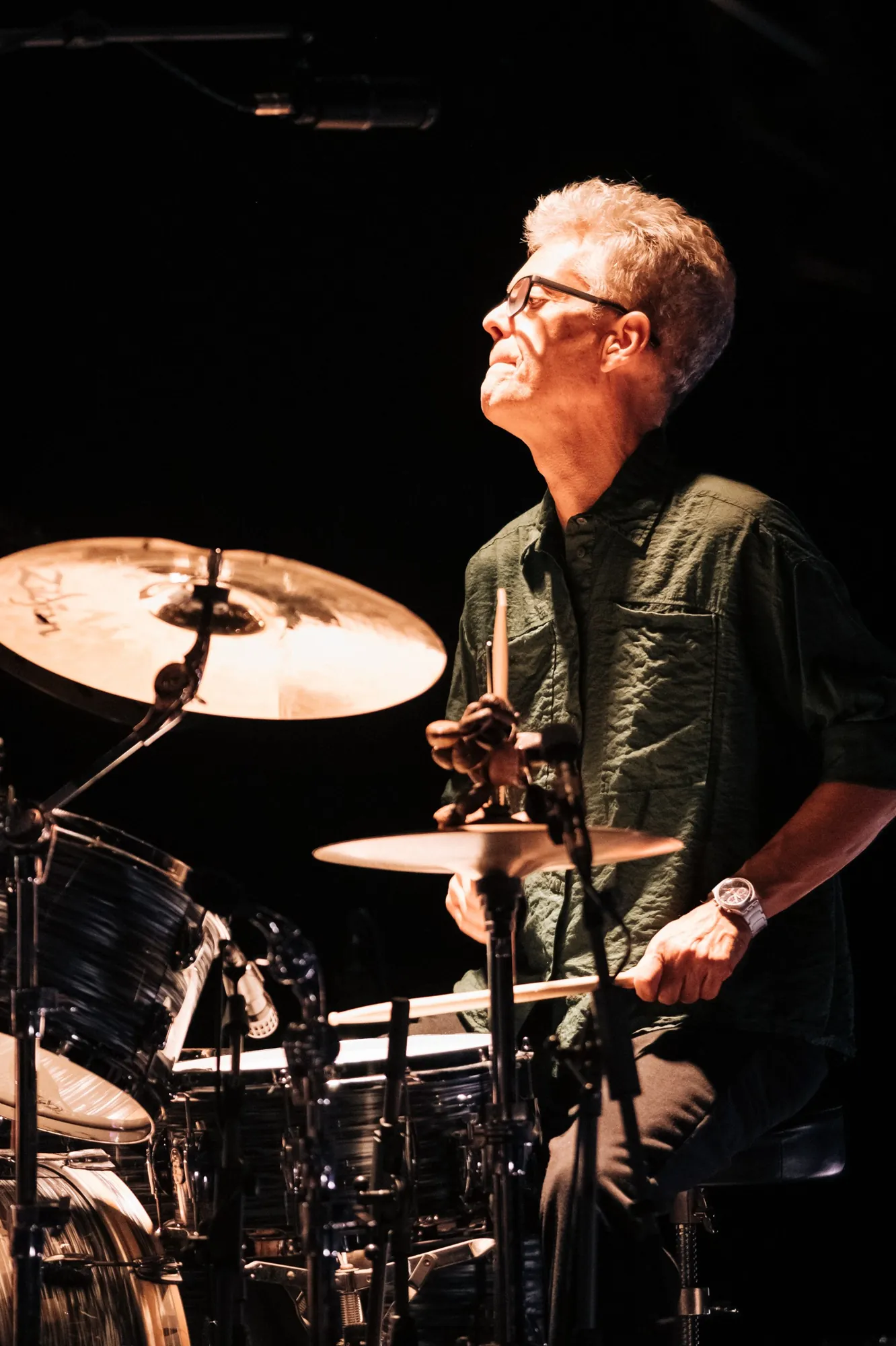 Baterista olha para cima durante o concerto, com os pratos em primeiro plano